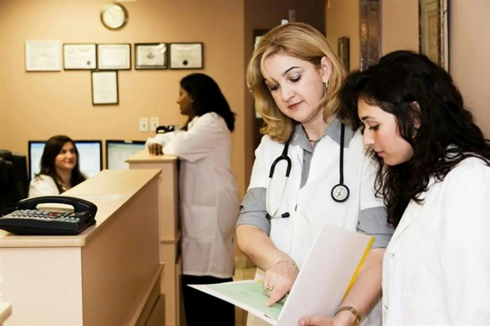 Two clinicians reviewing paperwork together near the front desk of a medical office